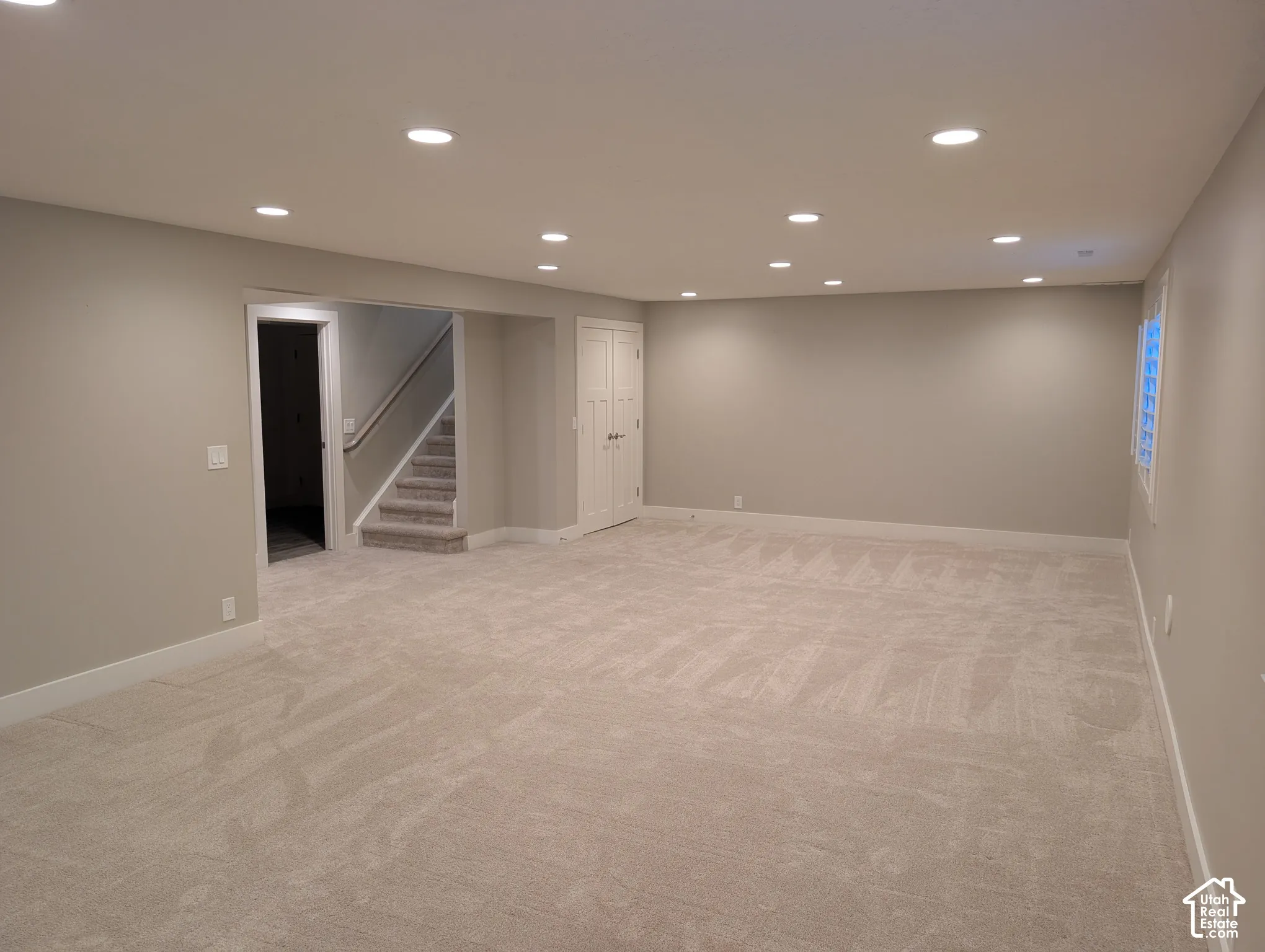 Spacious room with recessed lighting, light neutral-toned walls, light-toned carpeting, and a window with a white frame
