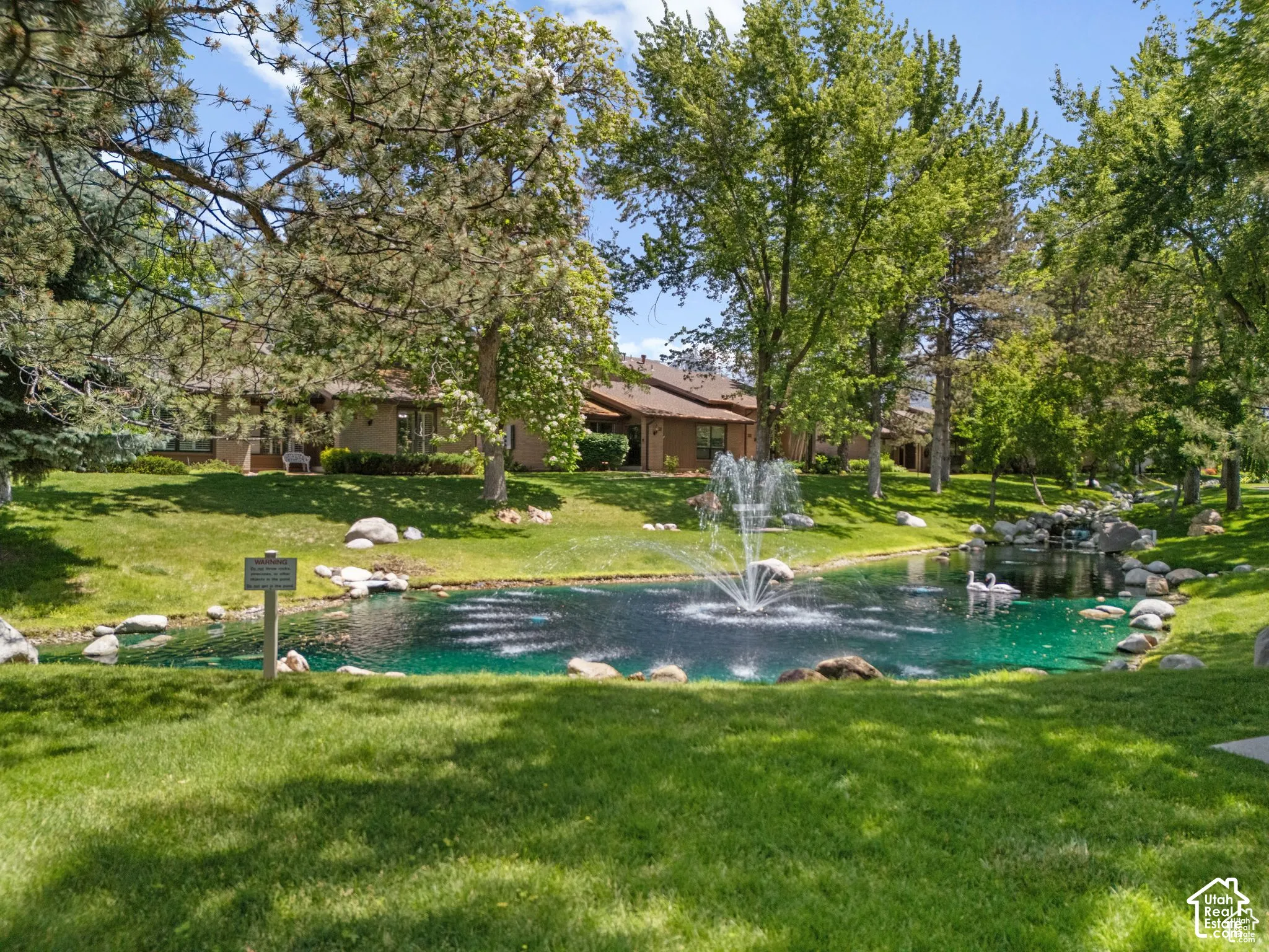 Landscaped grounds featuring a central pond with a fountain, surrounded by mature trees and manicured lawns