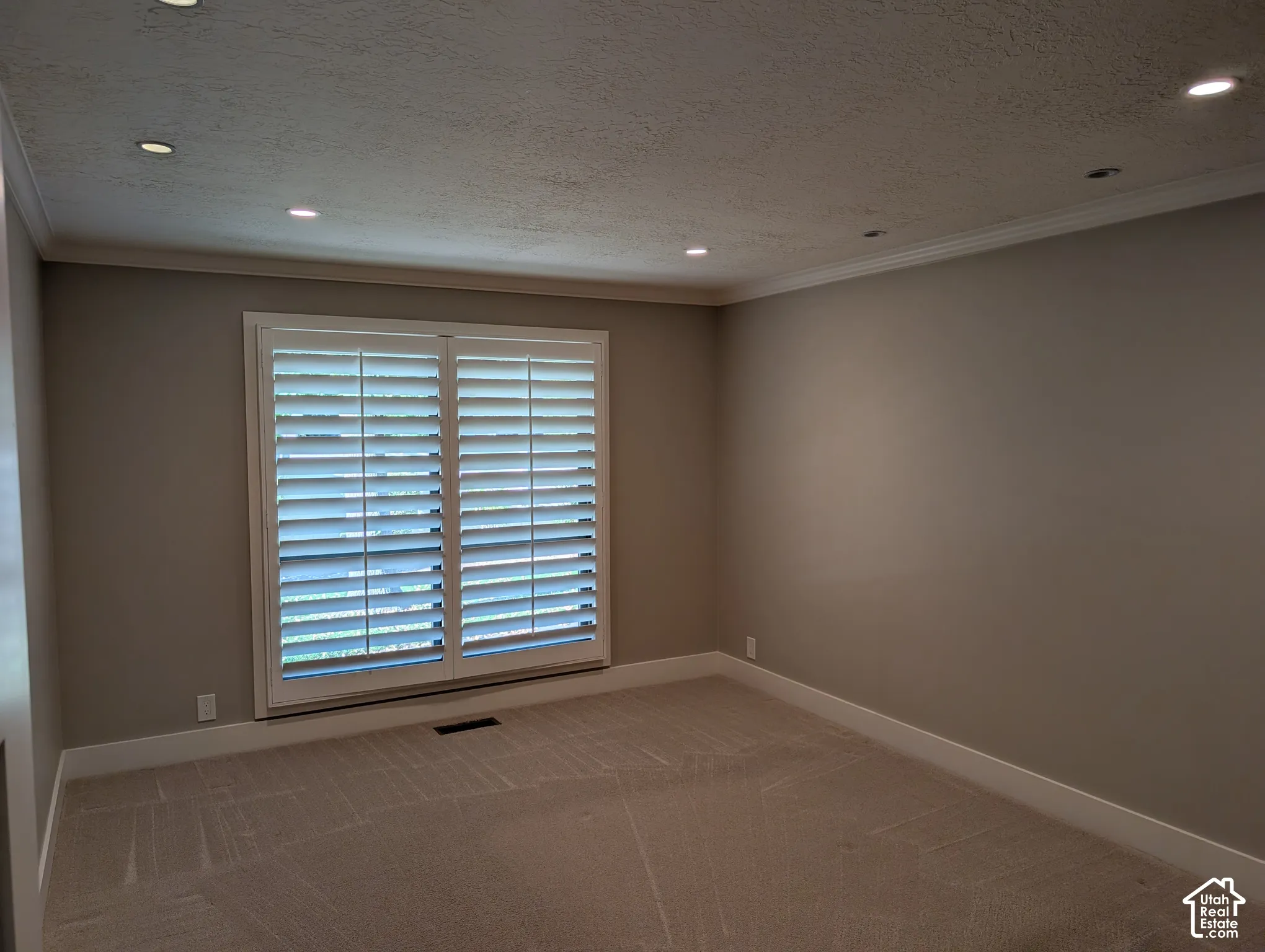Recessed lighting illuminates the space, featuring white crown molding and neutral wall tones