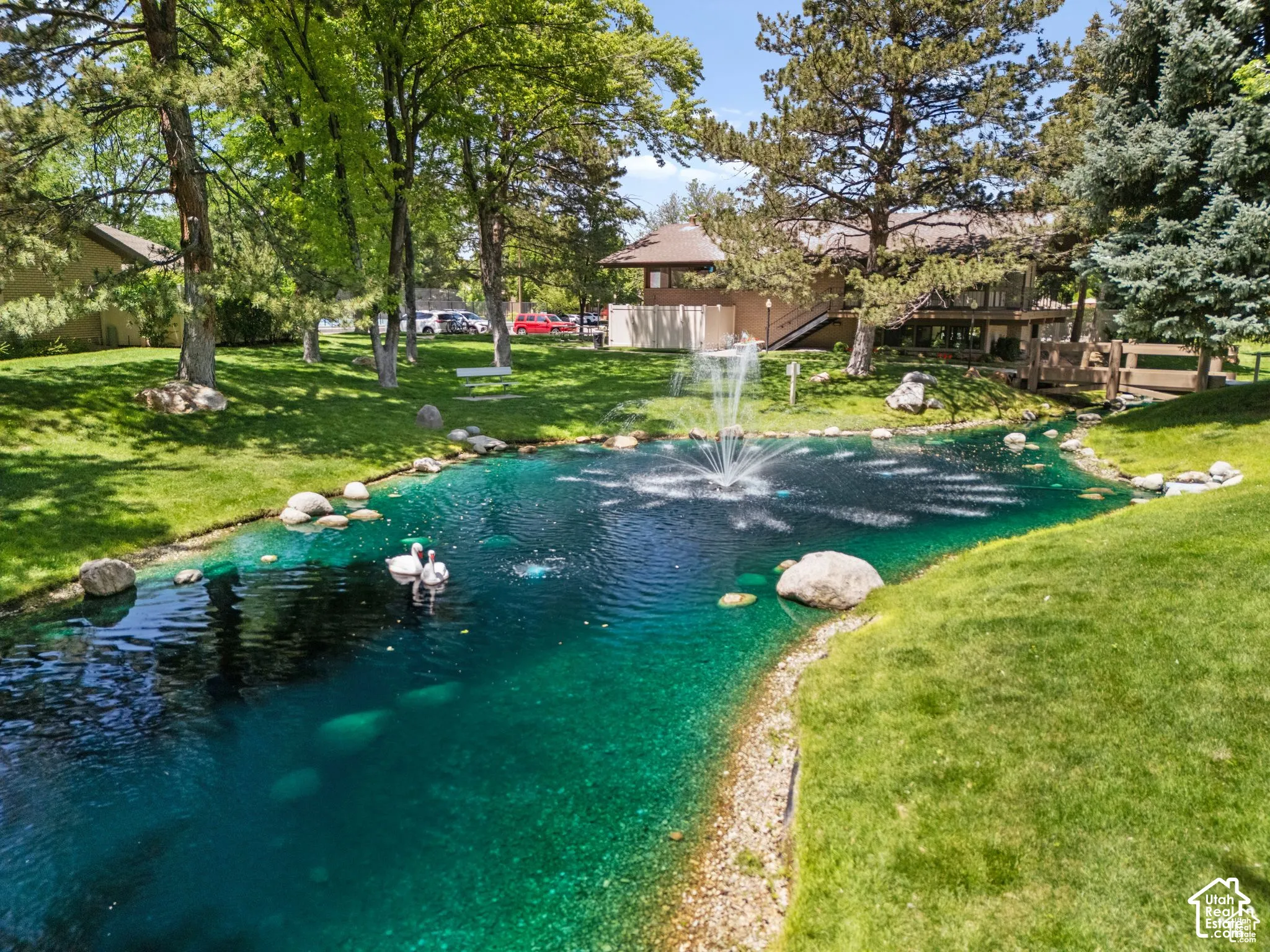 Water feature with a fountain, surrounded by manicured lawn and mature trees