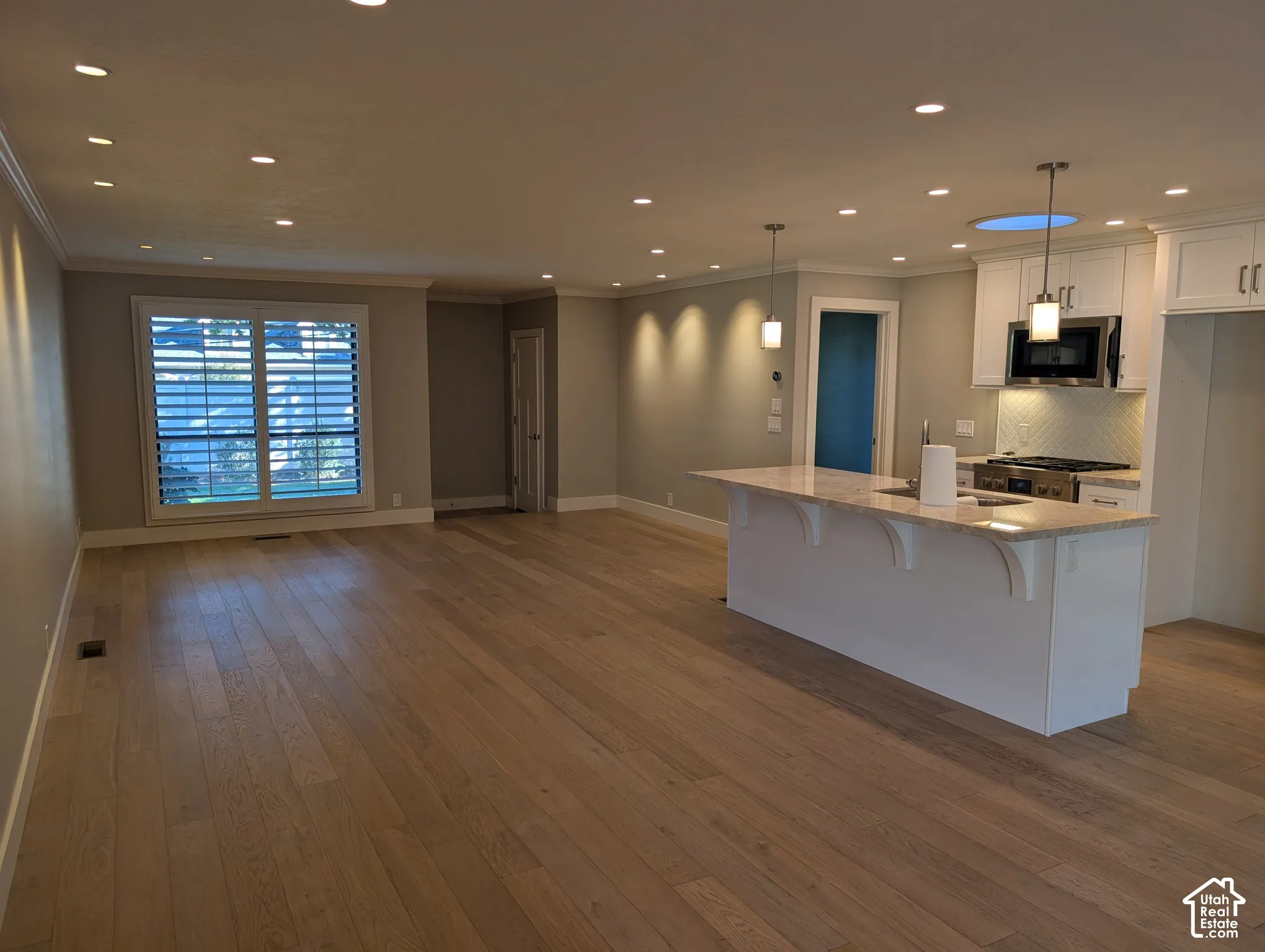 Wood-finish flooring throughout, white plantation shutters, recessed lighting, kitchen island with stone countertop, and stainless steel kitchen appliances