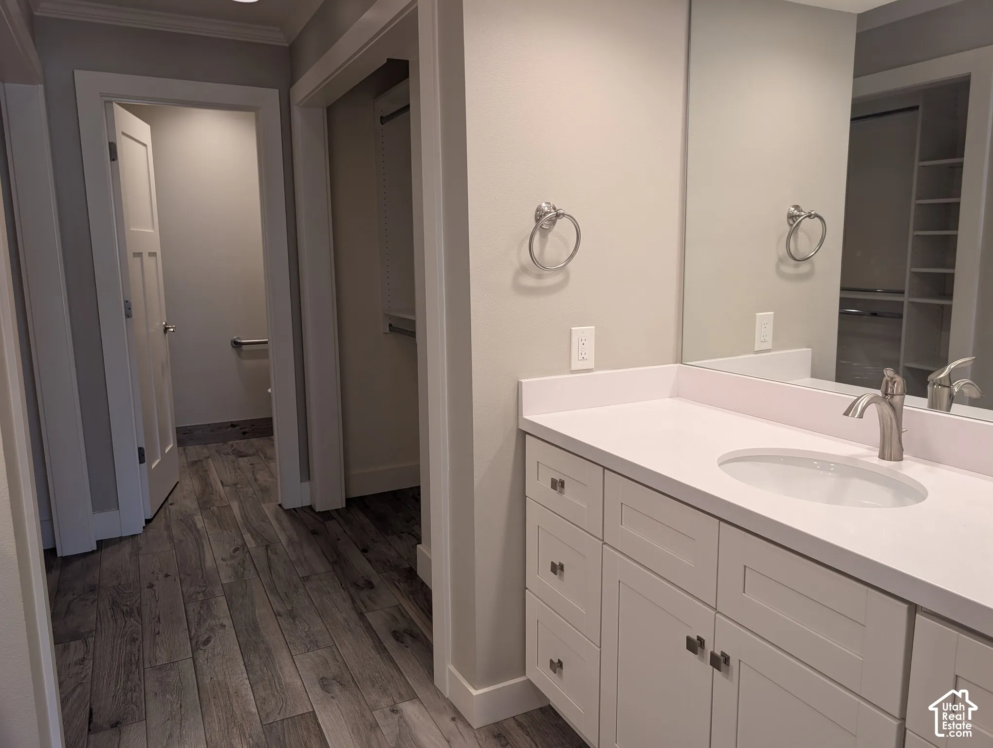 Wood-finish flooring throughout, white shaker vanity with dual sinks, brushed nickel fixtures, and a large wall-mounted mirror