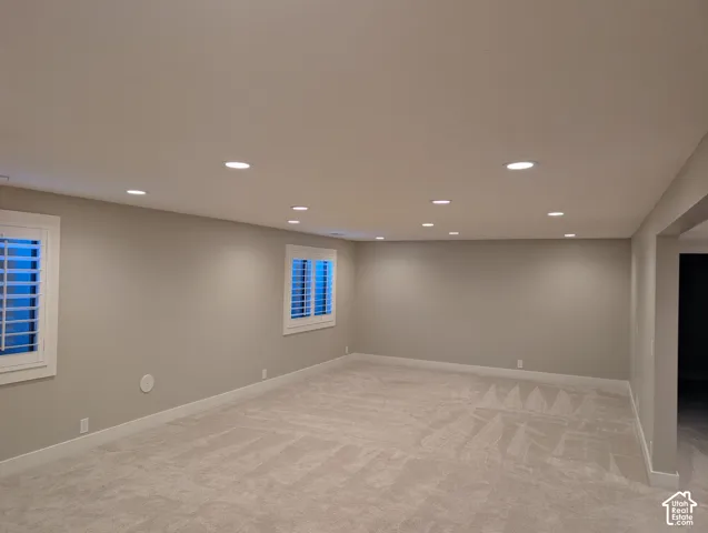 Recessed lighting, neutral wall tones, two windows with white plantation shutters, and light-toned carpet flooring