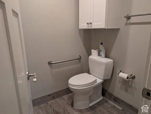 Wood-finish flooring, wall-mounted cabinetry, white toilet, and brushed nickel hardware