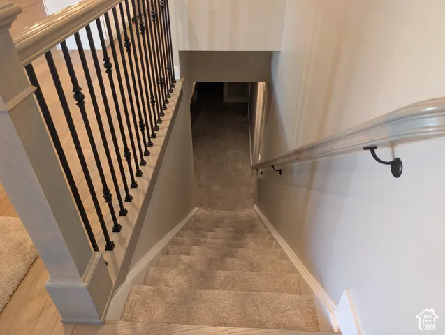 Carpeted staircase with light wood-finish handrail, wrought iron balusters, and white baseboards