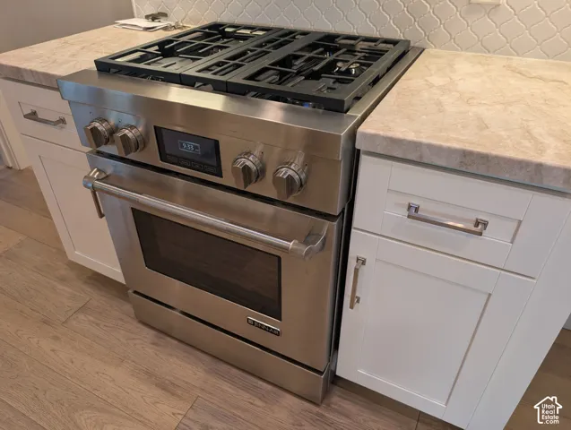 Stainless steel range with a gas cooktop, light-toned countertops, white shaker-style cabinetry, and wood-finish flooring