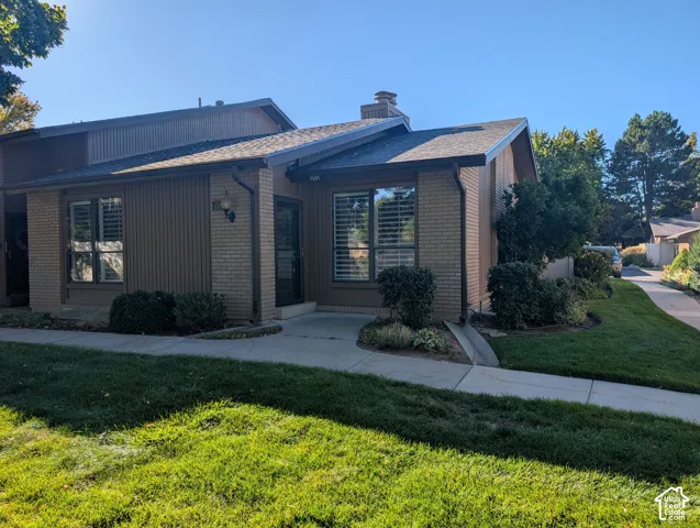 Brick and panel siding exterior with a concrete walkway, mature landscaping, and an asphalt shingle roof