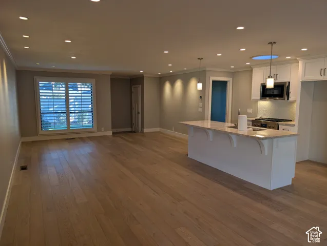 Wood-finish flooring throughout, white plantation shutters, recessed lighting, kitchen island with stone countertop, and stainless steel kitchen appliances