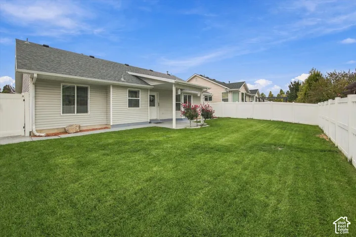 Expansive lawn area with a white privacy fence, a covered patio, and a light-colored siding exterior
