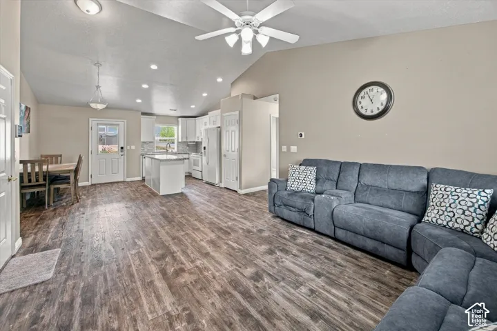 Vaulted ceilings with a ceiling fan, wood-finish flooring, recessed lighting, white kitchen cabinetry with a tile backsplash, and a kitchen island with seating