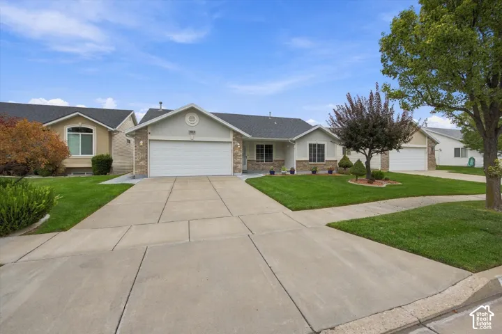 Single-story residence featuring a concrete driveway, attached garage, and front yard with mature trees