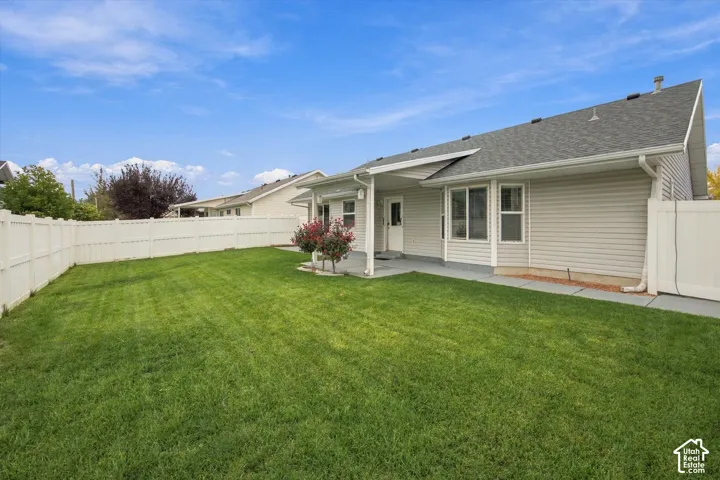 Expansive green lawn with a full white privacy fence, a covered patio, and light-colored siding