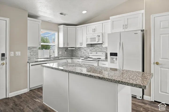 Kitchen featuring wood-finish flooring, white cabinetry, a kitchen island with stone-finish countertop, a tile backsplash, and a window with blinds