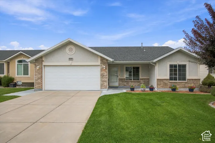 Property exterior featuring stucco and brick accents, an attached garage, a paved driveway, and a front lawn