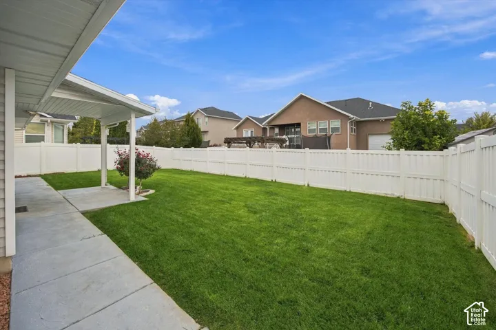 Expansive backyard featuring a manicured lawn, full privacy fencing, concrete patio, and a covered porch