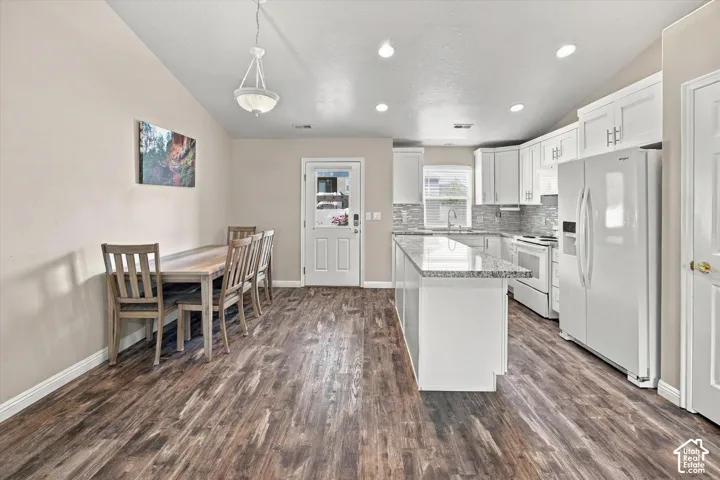 Wood-finish flooring, white cabinetry, a kitchen island with stone-look countertop, a tile backsplash, and recessed lighting