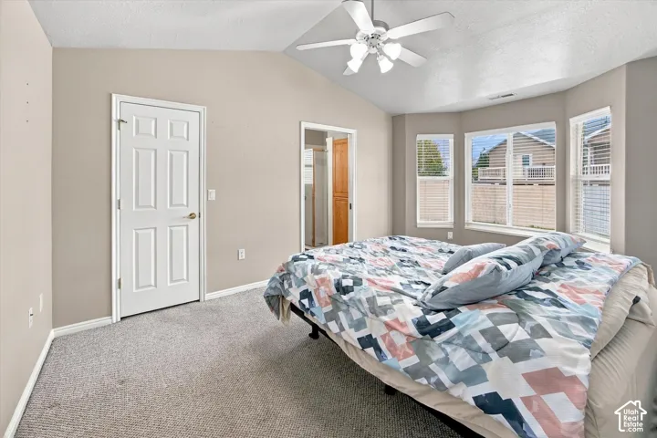 Vaulted ceiling with ceiling fan, bay window with blinds, light gray wall paint, and gray carpet flooring