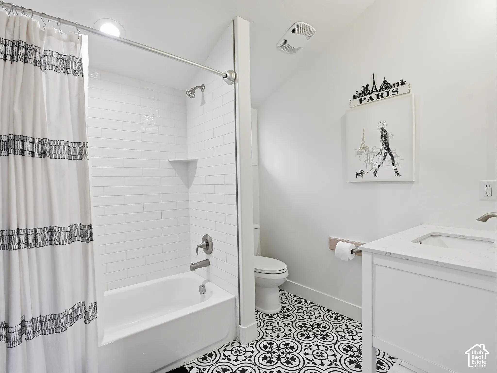 Bathroom featuring a white vanity with a stone countertop, subway-tiled tub surround, and patterned tile flooring