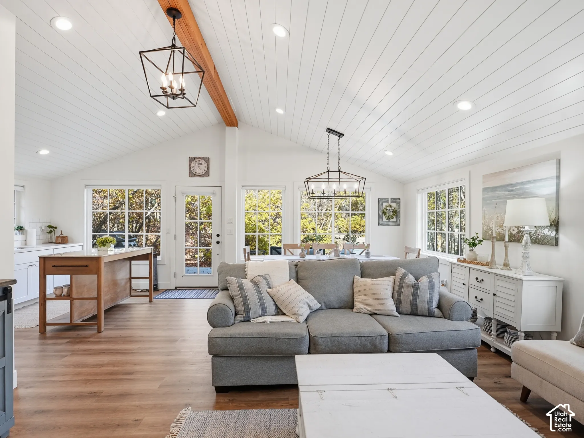 Vaulted ceilings featuring white shiplap paneling and a natural wood beam, wood-finish flooring, multi-pane windows, and geometric metal pendant lighting