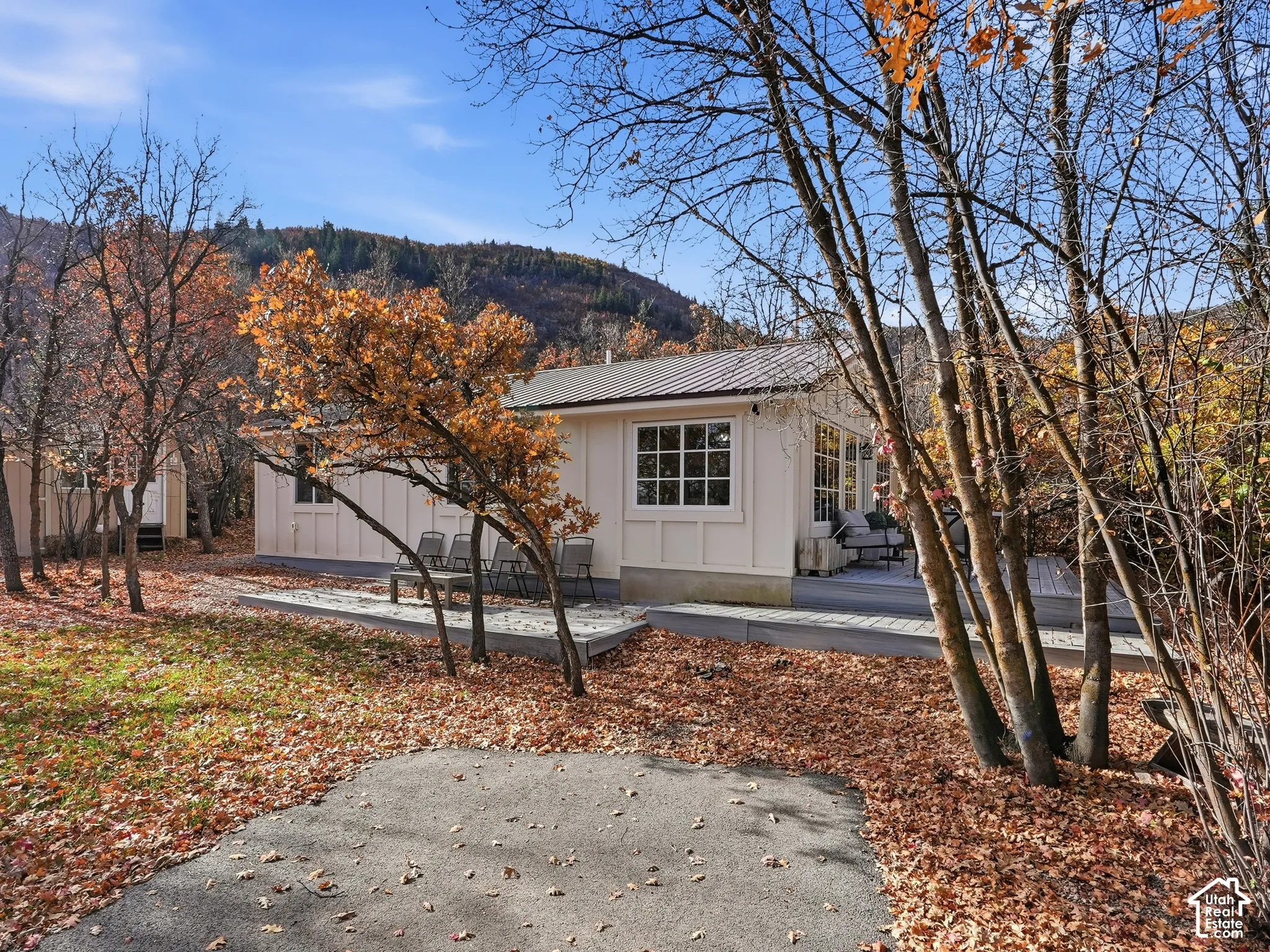 Exterior featuring board-and-batten siding, a metal roof, multi-pane windows, and a wraparound wooden deck set against a mountain backdrop