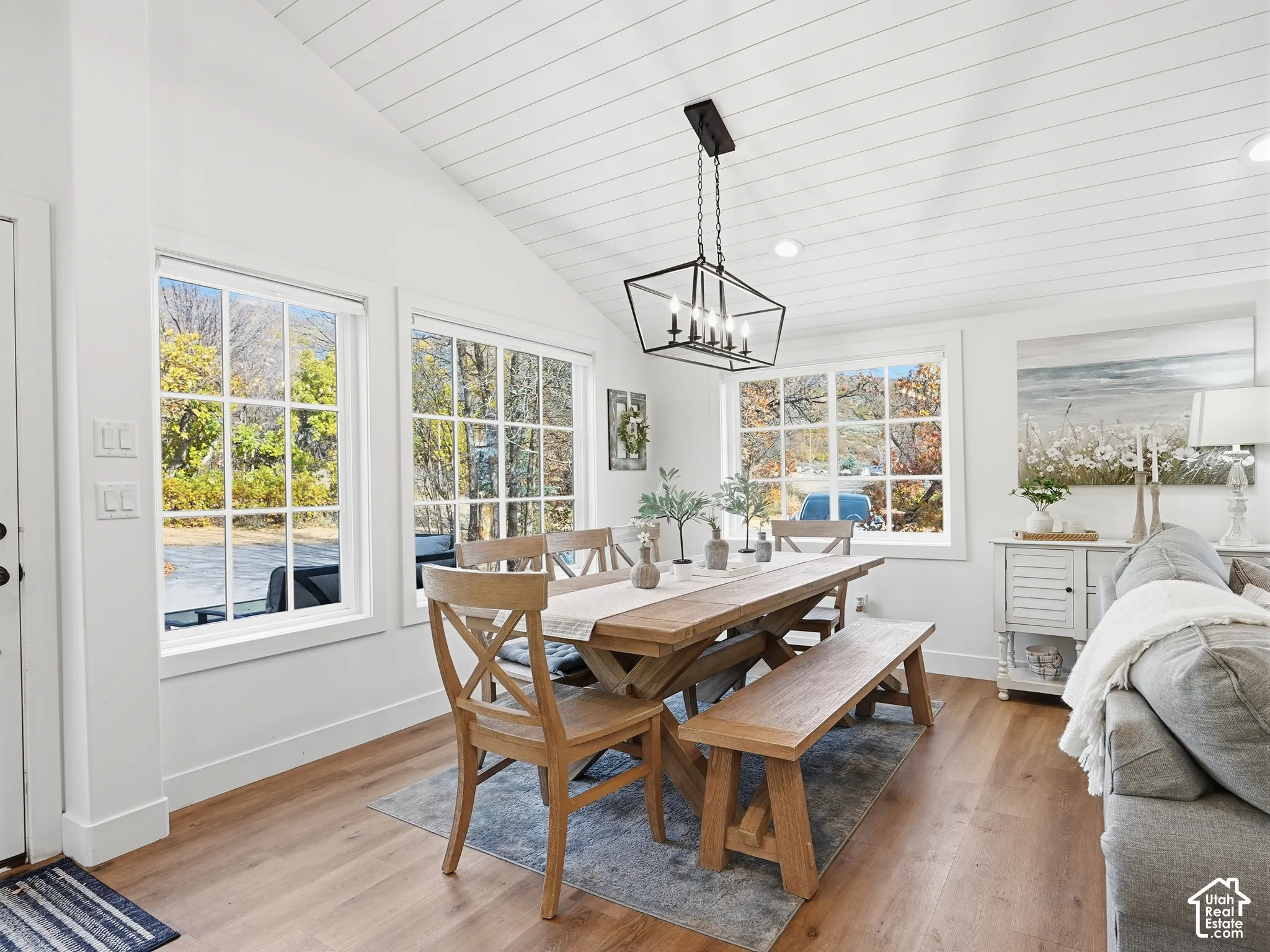 Vaulted ceilings with white shiplap paneling, wood-finish flooring, large multi-pane windows, and a geometric black metal chandelier
