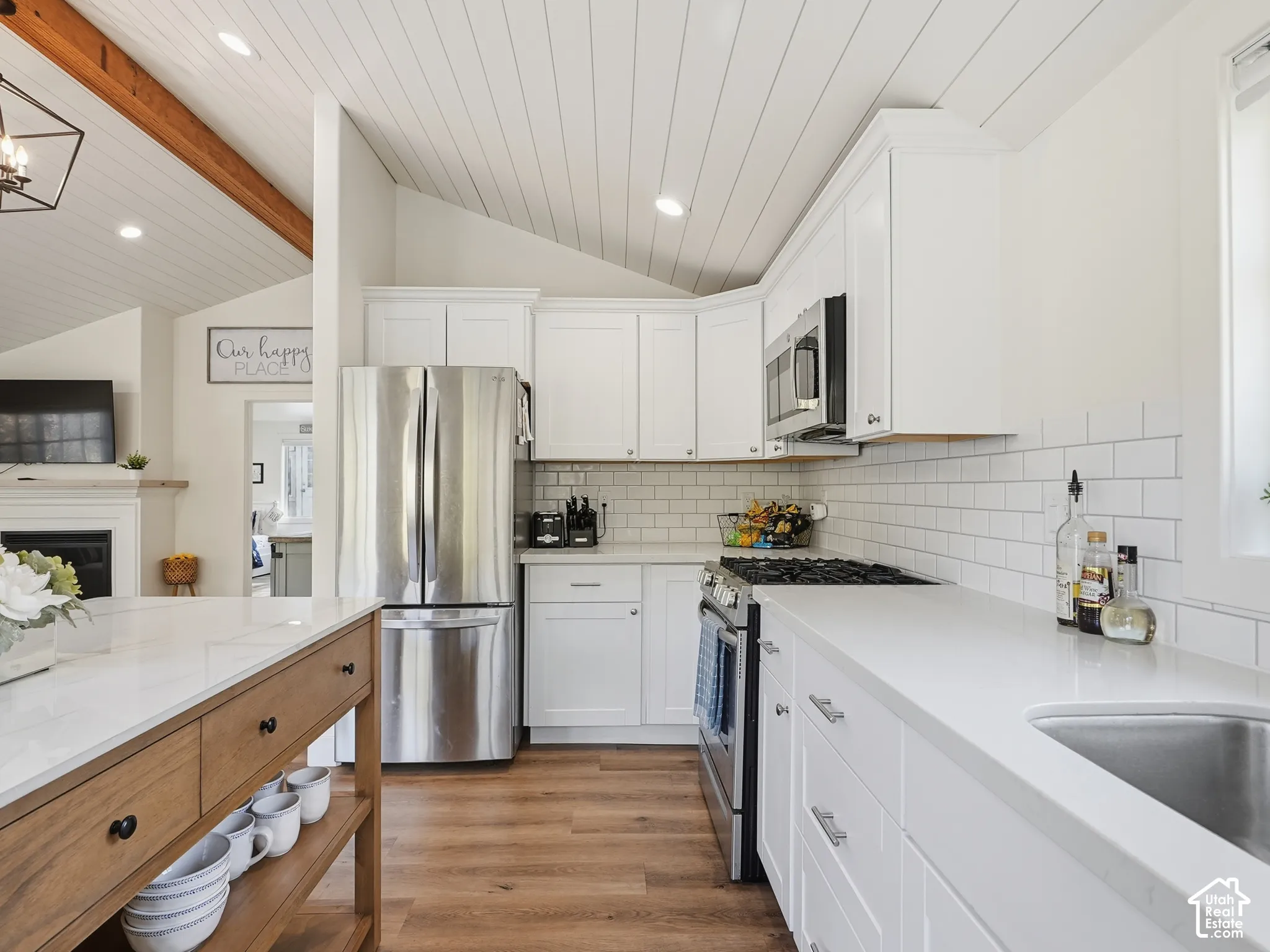Kitchen featuring white shaker-style cabinetry, solid-surface countertops, subway tile backsplash, wood-finish flooring, and a vaulted ceiling with exposed wooden beams