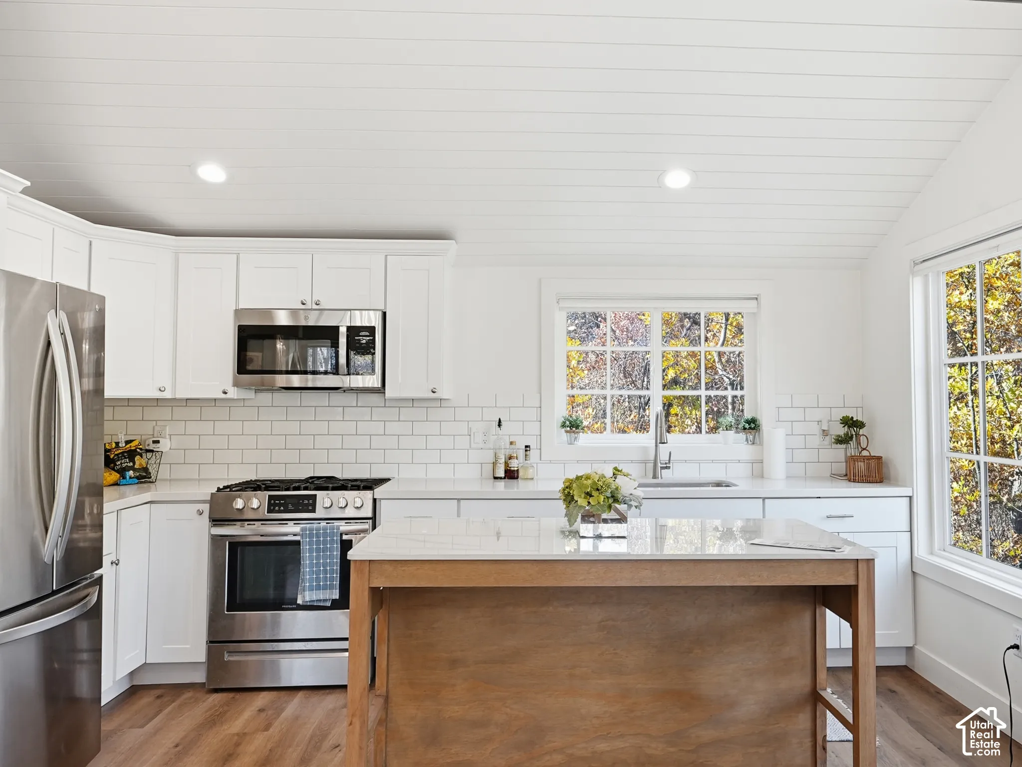 Kitchen featuring white shaker-style cabinetry, white subway tile backsplash, light stone-finish countertops, wood-finish center island, and wood-finish flooring under a vaulted shiplap ceiling