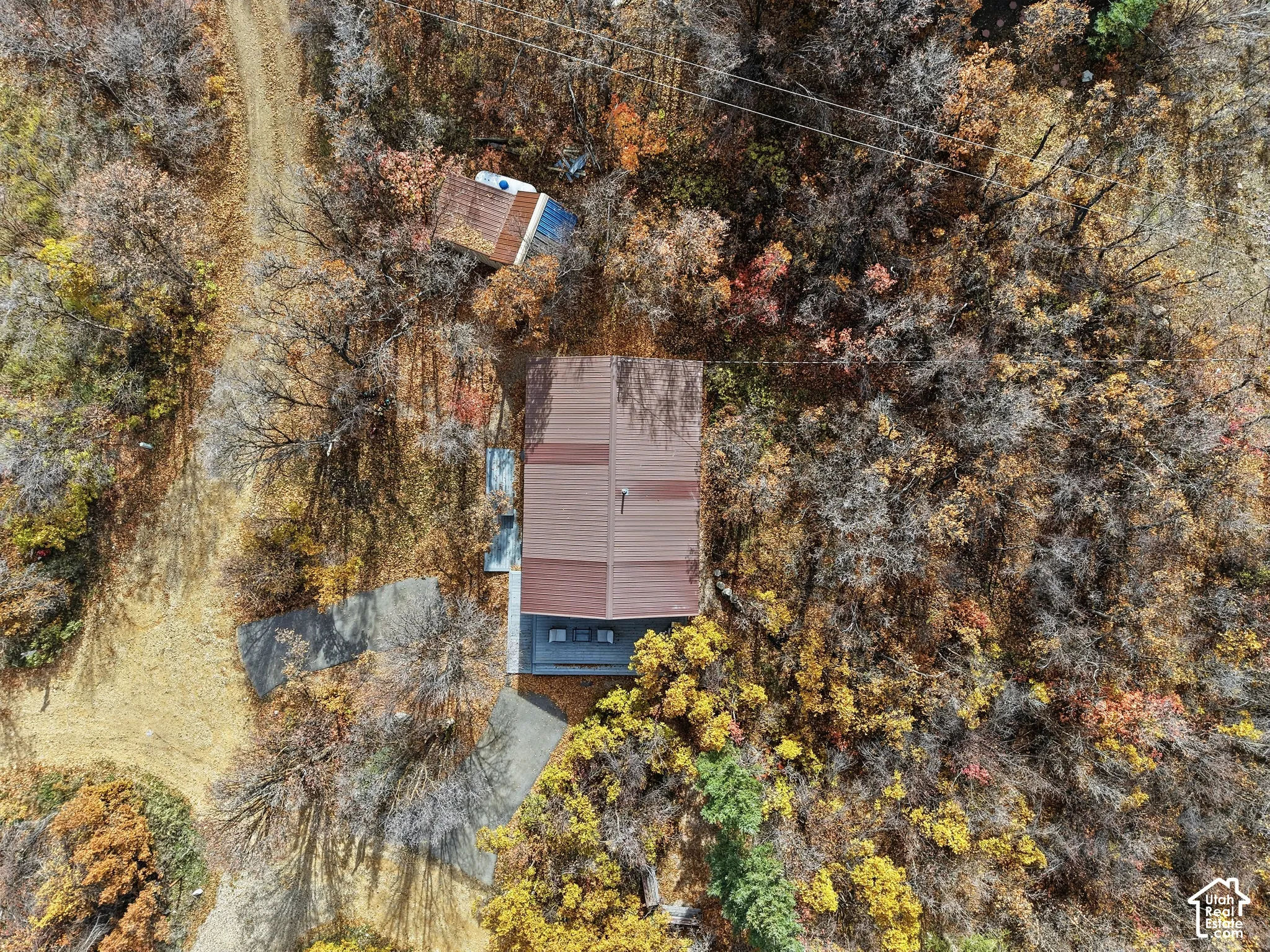 Aerial perspective featuring a metal roof structure, paved driveway, detached outbuilding, and mature wooded acreage