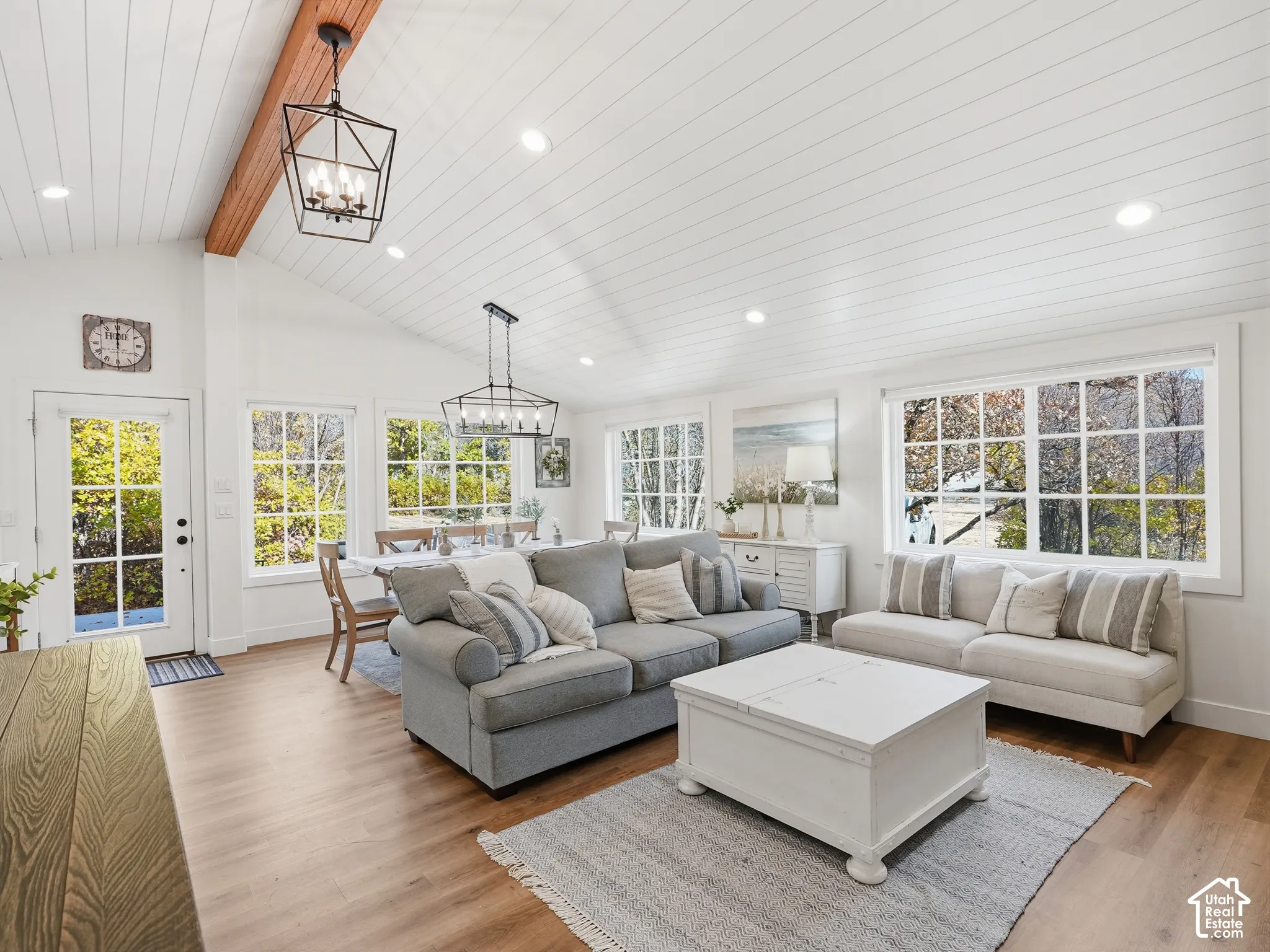 Vaulted ceilings with plank-style paneling, exposed natural wood beam, geometric metal chandeliers, wood-finish flooring, and expansive windows with muntin detailing