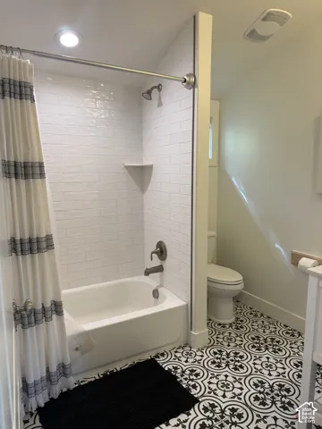 White subway tile shower surround, built-in shower shelf, brushed bronze bath fixtures, patterned tile flooring, and integrated ceiling lighting