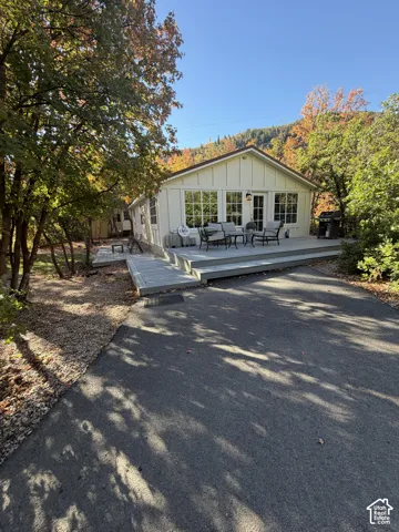 White board and batten siding, multiple pane windows, a covered deck, and an asphalt driveway