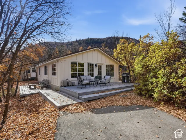 Single-story exterior featuring vertical siding, grid-pattern windows, multi-level wood decking, and mountainous backdrop