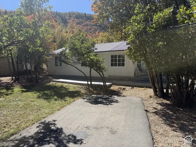 White exterior with a dark metal roof, multiple windows, concrete patio, and a gravel driveway