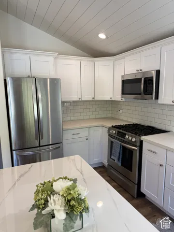 Vaulted ceiling with shiplap finish, white shaker-style cabinetry, stainless steel appliances, subway tile backsplash, and wood-finish flooring