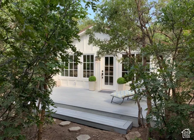 White board and batten siding, multiple pane windows, a glass-paned door, and a light gray deck with steps