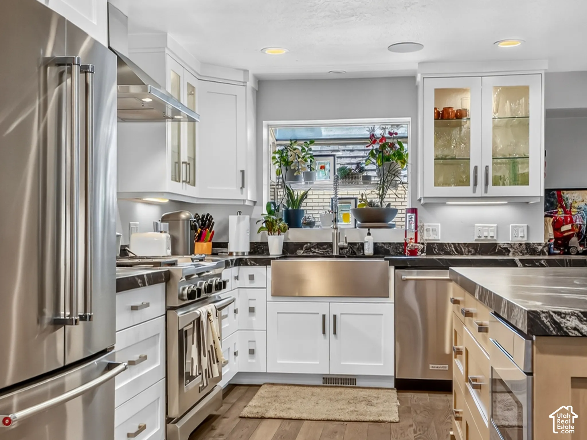 Gourmet kitchen featuring stainless steel appliances, recessed lighting, wood-finish flooring, white cabinetry, and contrasting stone countertops