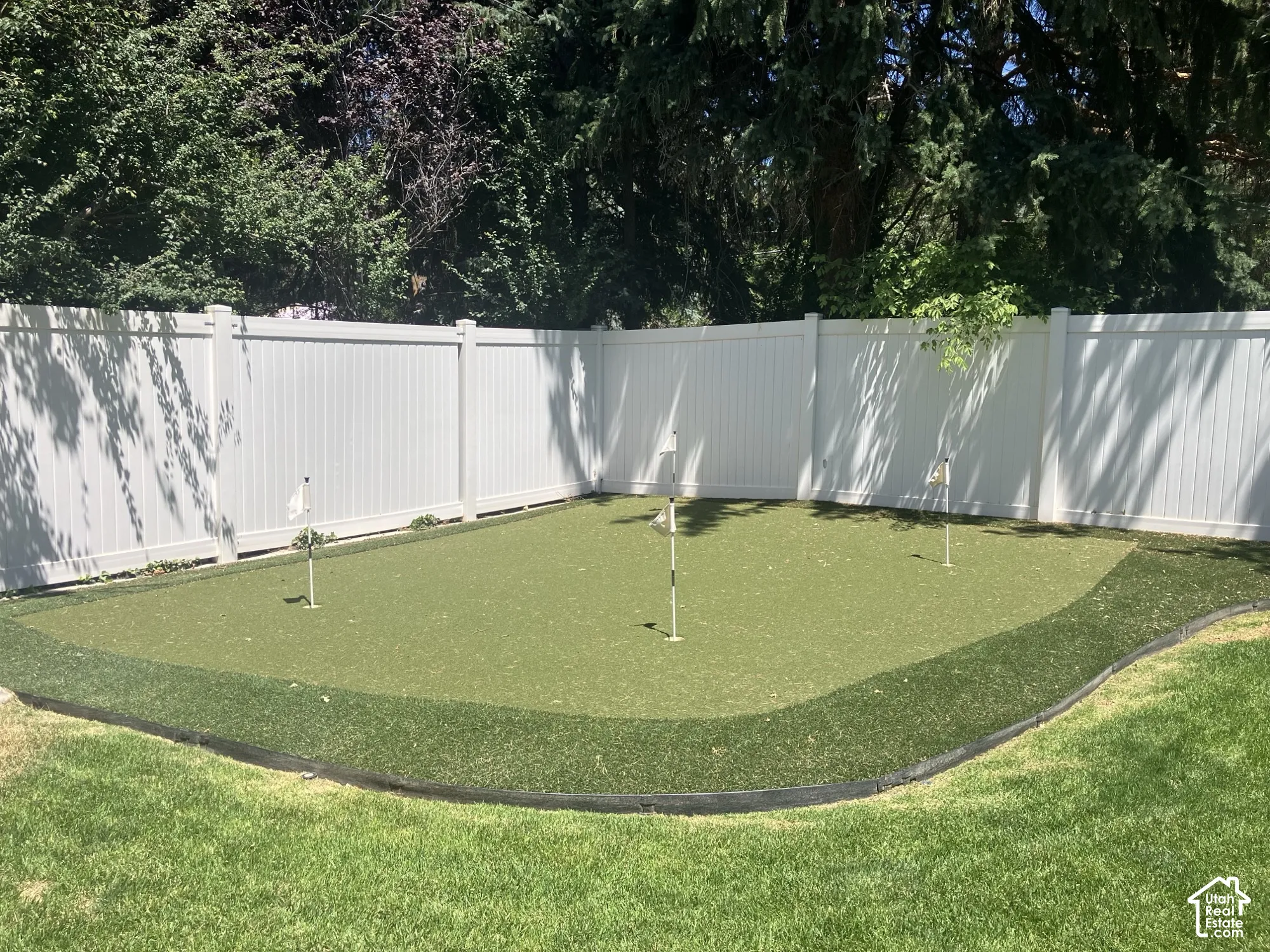 Putting green with multiple holes, artificial turf, and a white vinyl fence