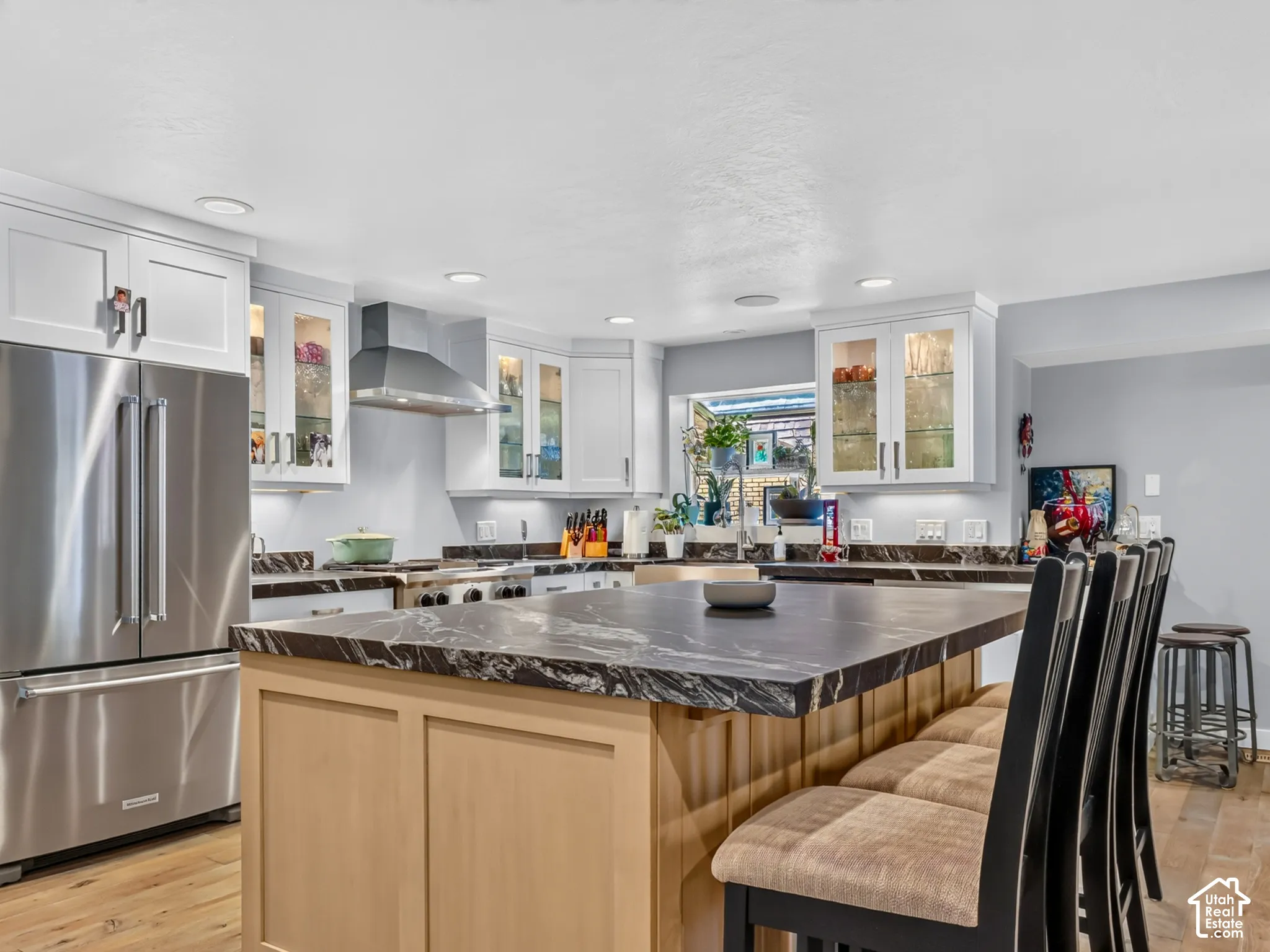 Kitchen featuring a large central island with a dark stone countertop, light wood-finish flooring, white cabinetry with glass inserts, stainless steel appliances, and recessed lighting