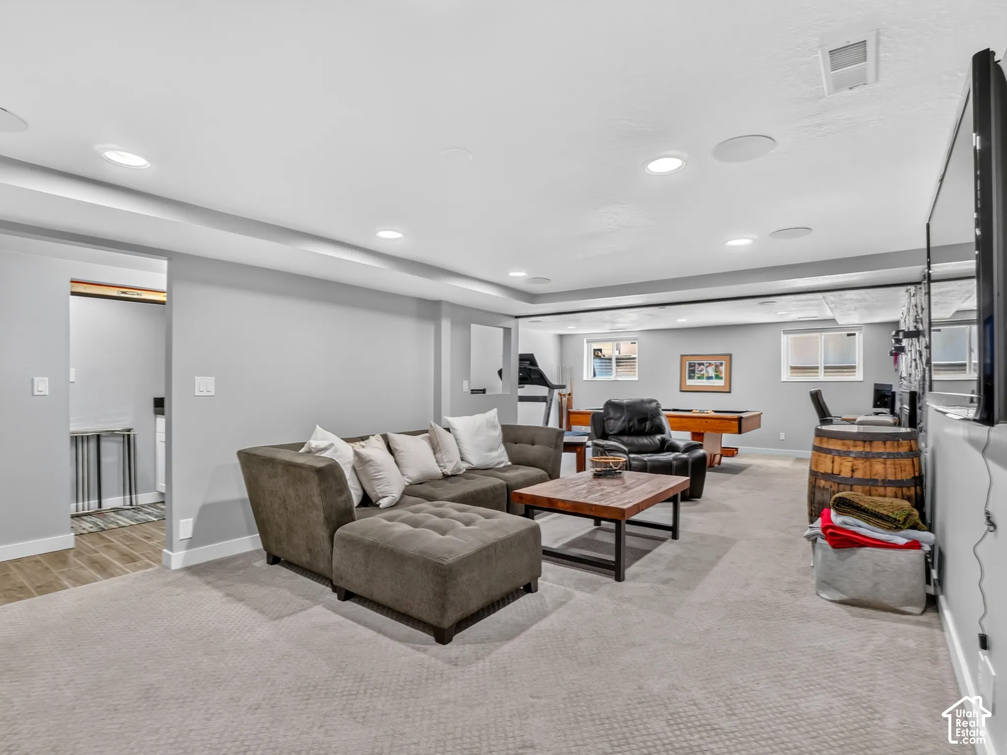 Recessed lighting, wall-mounted television, and light-toned carpet flooring