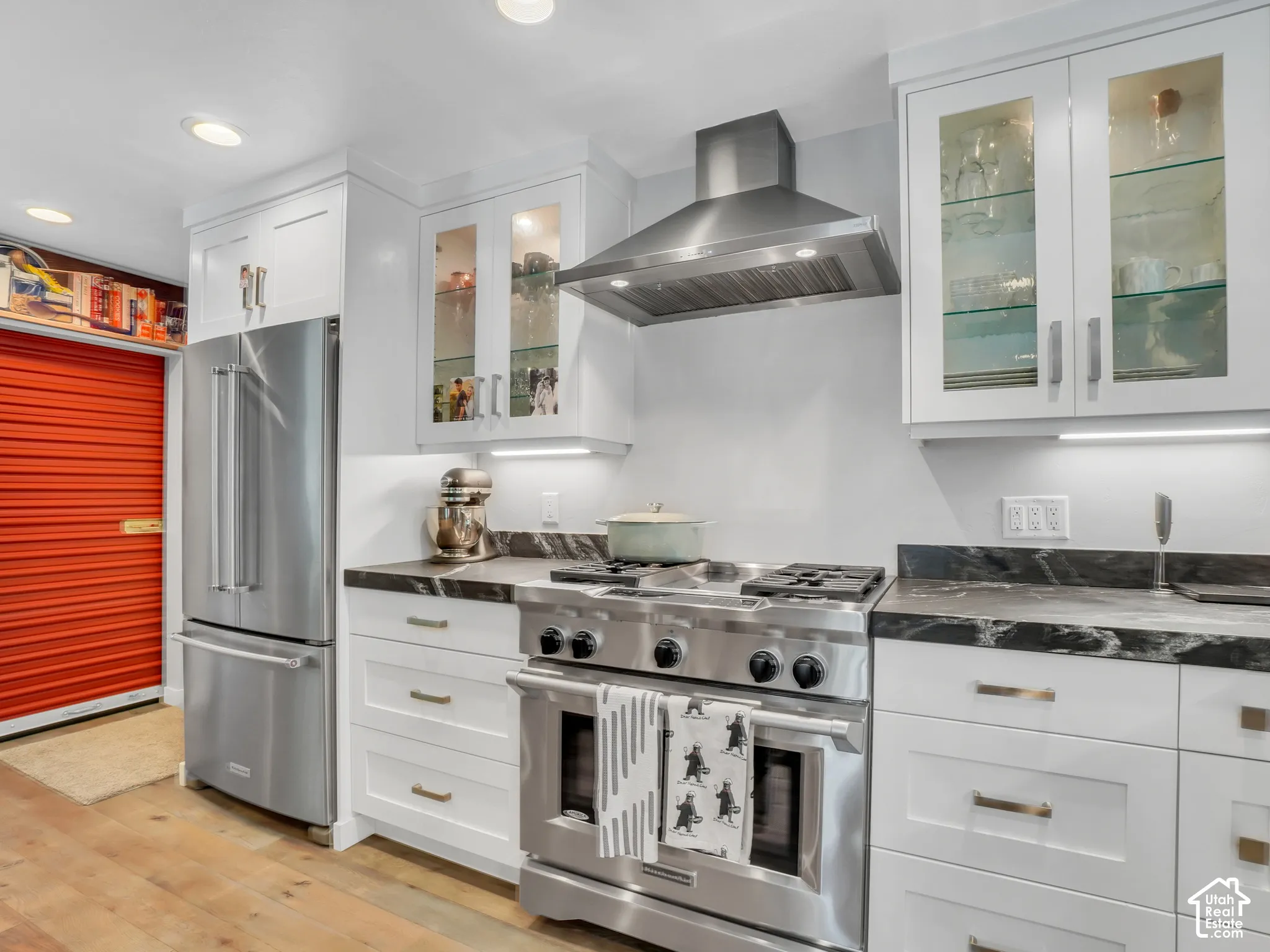 White shaker cabinetry with glass-front upper cabinets, stainless steel appliances, dark stone countertops, and wood-finish flooring