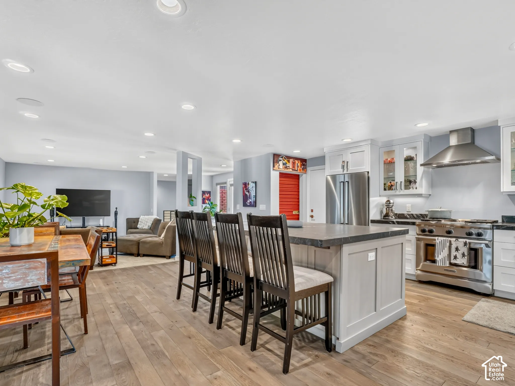 Wood-finish flooring throughout, kitchen island with counter seating, stainless steel appliances, white cabinetry with glass-front accents, and recessed lighting