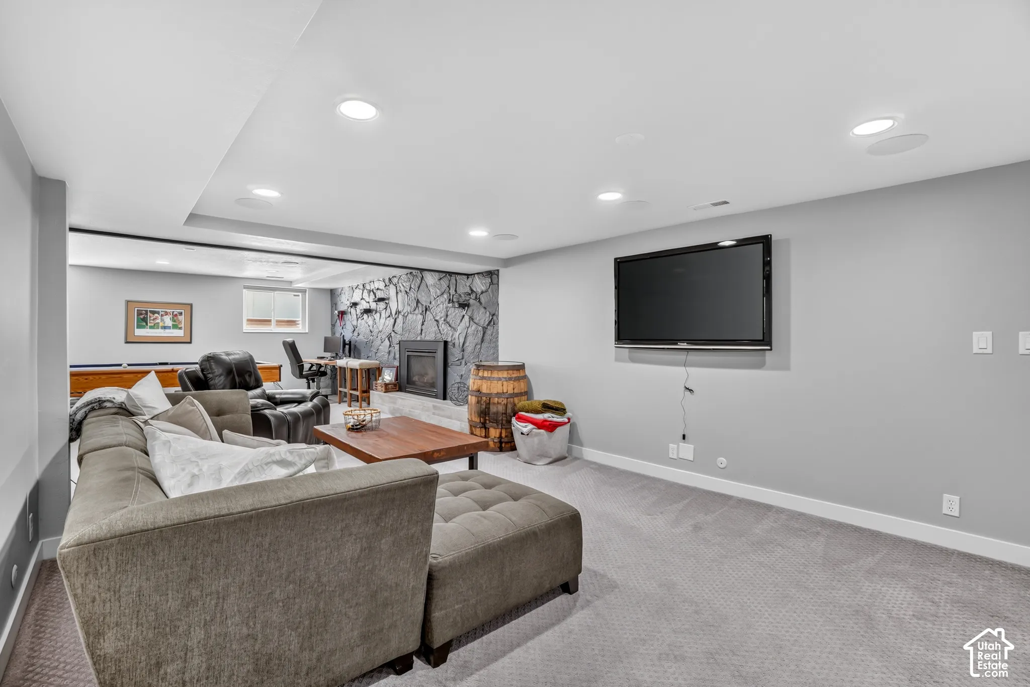 Recessed ceiling lighting, integrated ceiling speakers, wall-mounted television, stone fireplace surround, and built-in shelving