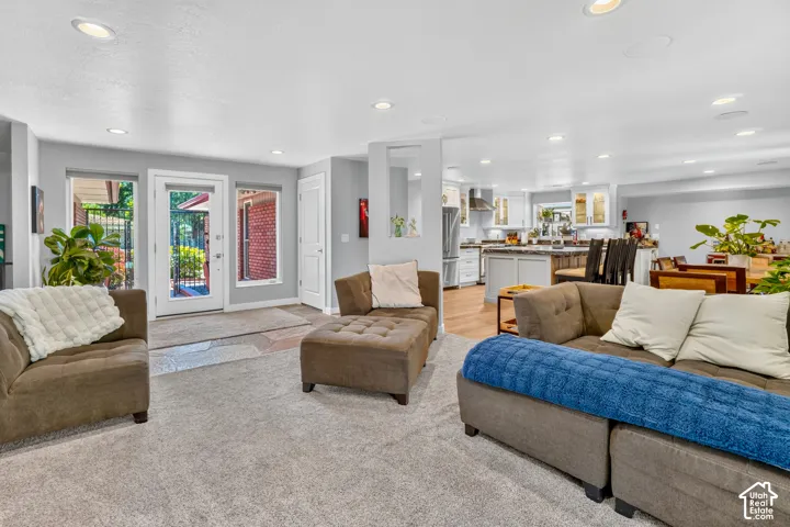 Recessed lighting, light gray carpet, and a kitchen with light-finish cabinetry, stainless steel appliances, and wood-finish flooring