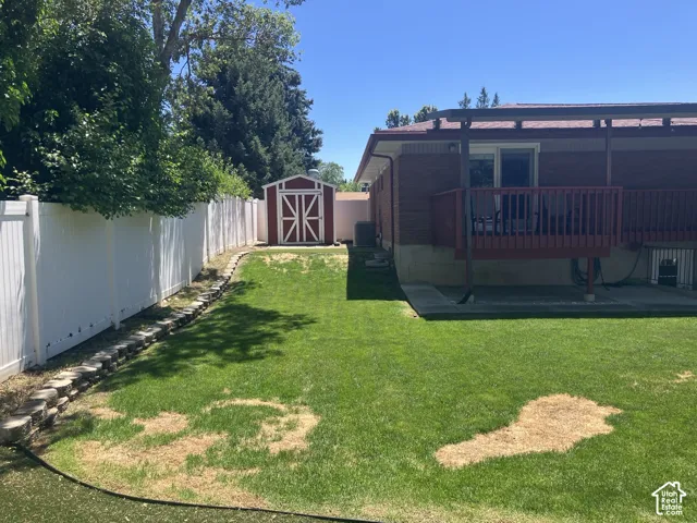 Private backyard featuring a white privacy fence, a storage shed, and an elevated deck with a covered patio below