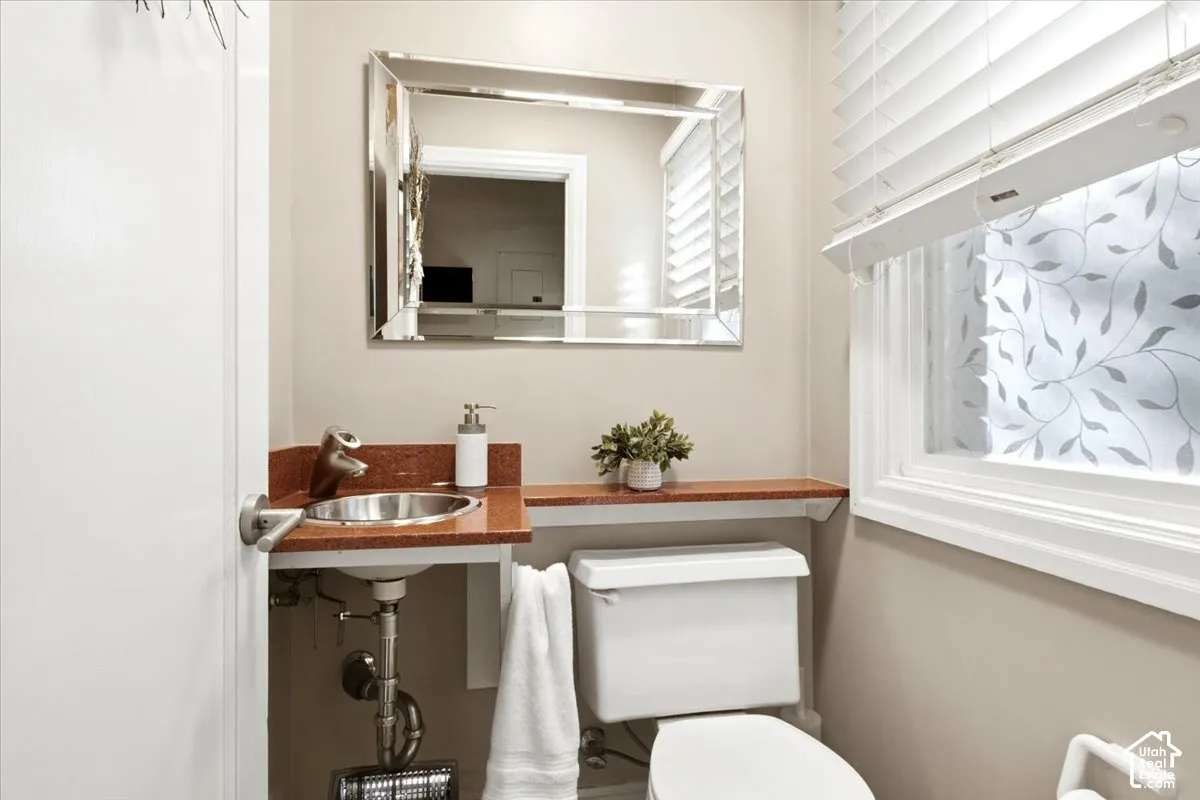 Compact powder room featuring a wall-mounted sink, a vanity mirror with a decorative frame, a window with privacy film, and a built-in shelf