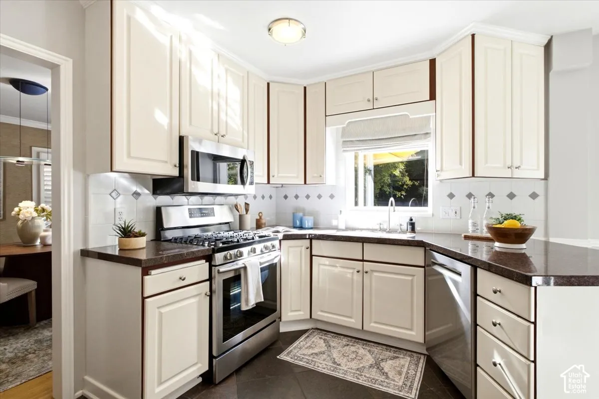 Kitchen featuring cream cabinetry, stainless steel appliances, granite countertops, and a decorative tile backsplash