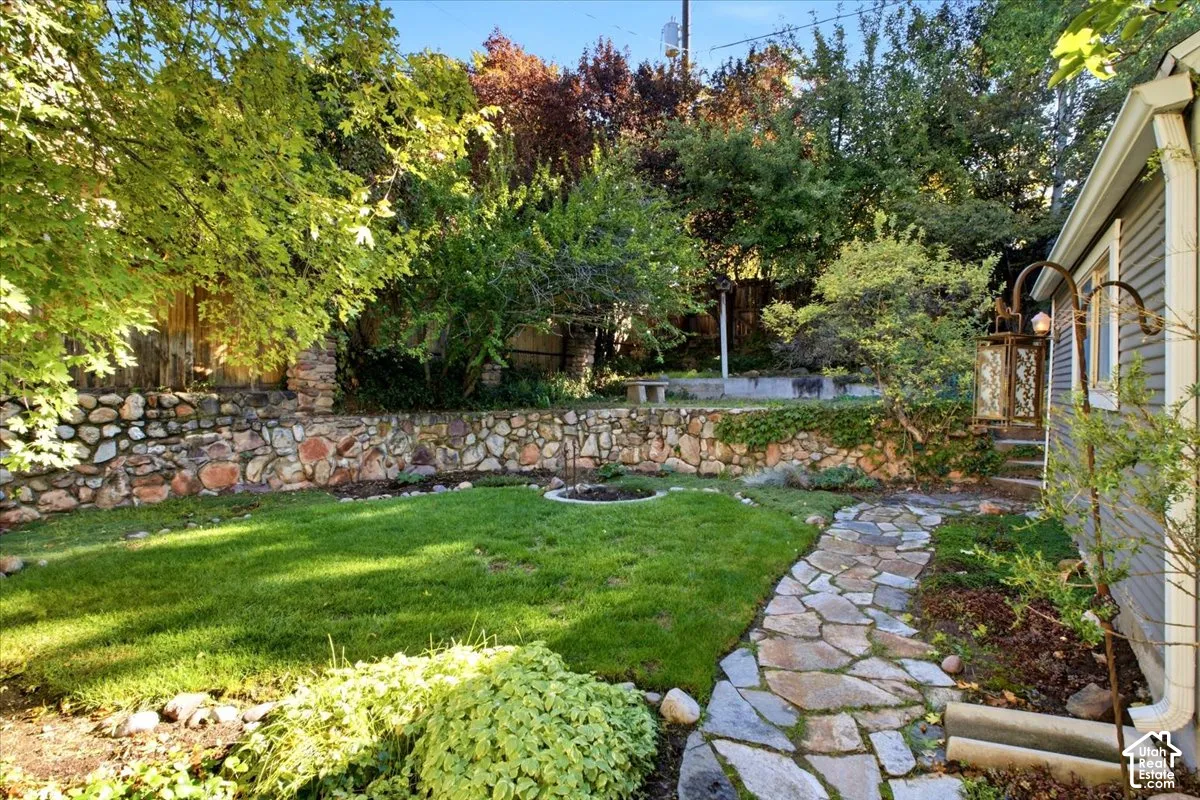 Expansive backyard featuring a manicured lawn, stone retaining walls, mature trees, and a flagstone pathway