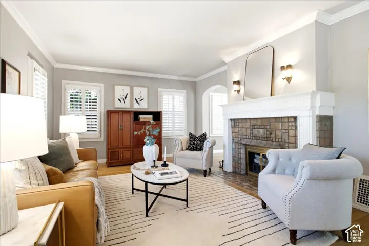 Hardwood flooring, crown molding, plantation shutters, and a terra cotta tiled fireplace with a substantial mantel