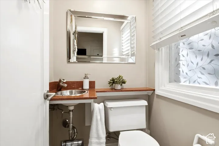 Compact powder room featuring a wall-mounted sink, a vanity mirror with a decorative frame, a window with privacy film, and a built-in shelf