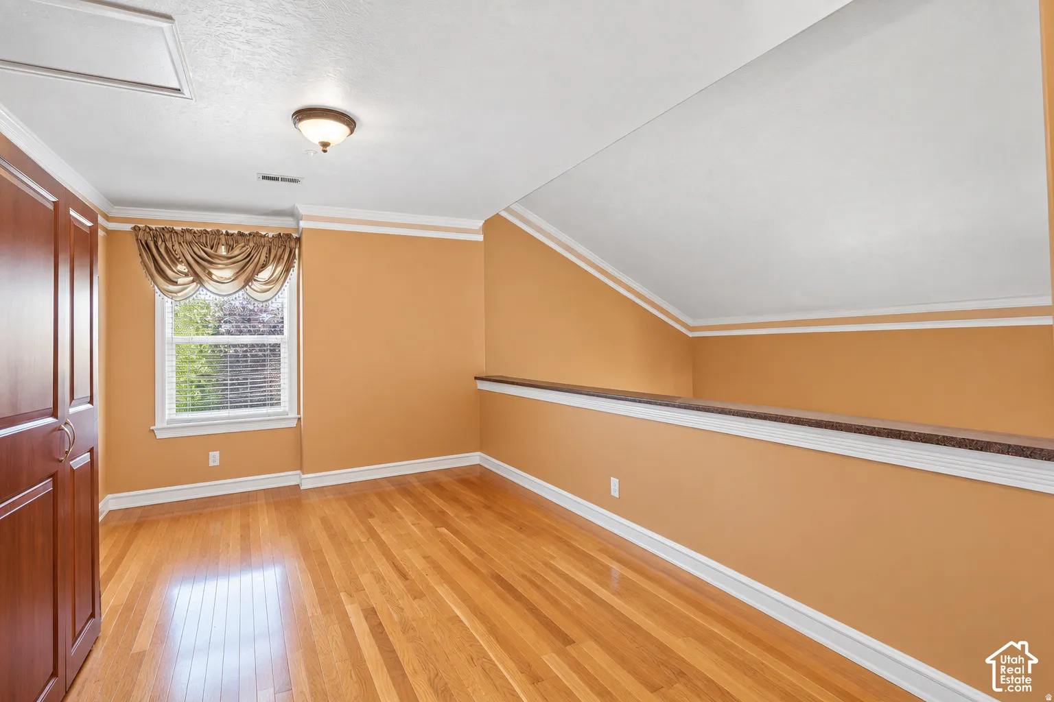 Hardwood flooring, built-in cabinetry, window with blinds, ceiling-mounted light fixture, and crown molding